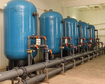 Row of blue pressure vessels with grey pipework and orange valves in a process water plant room